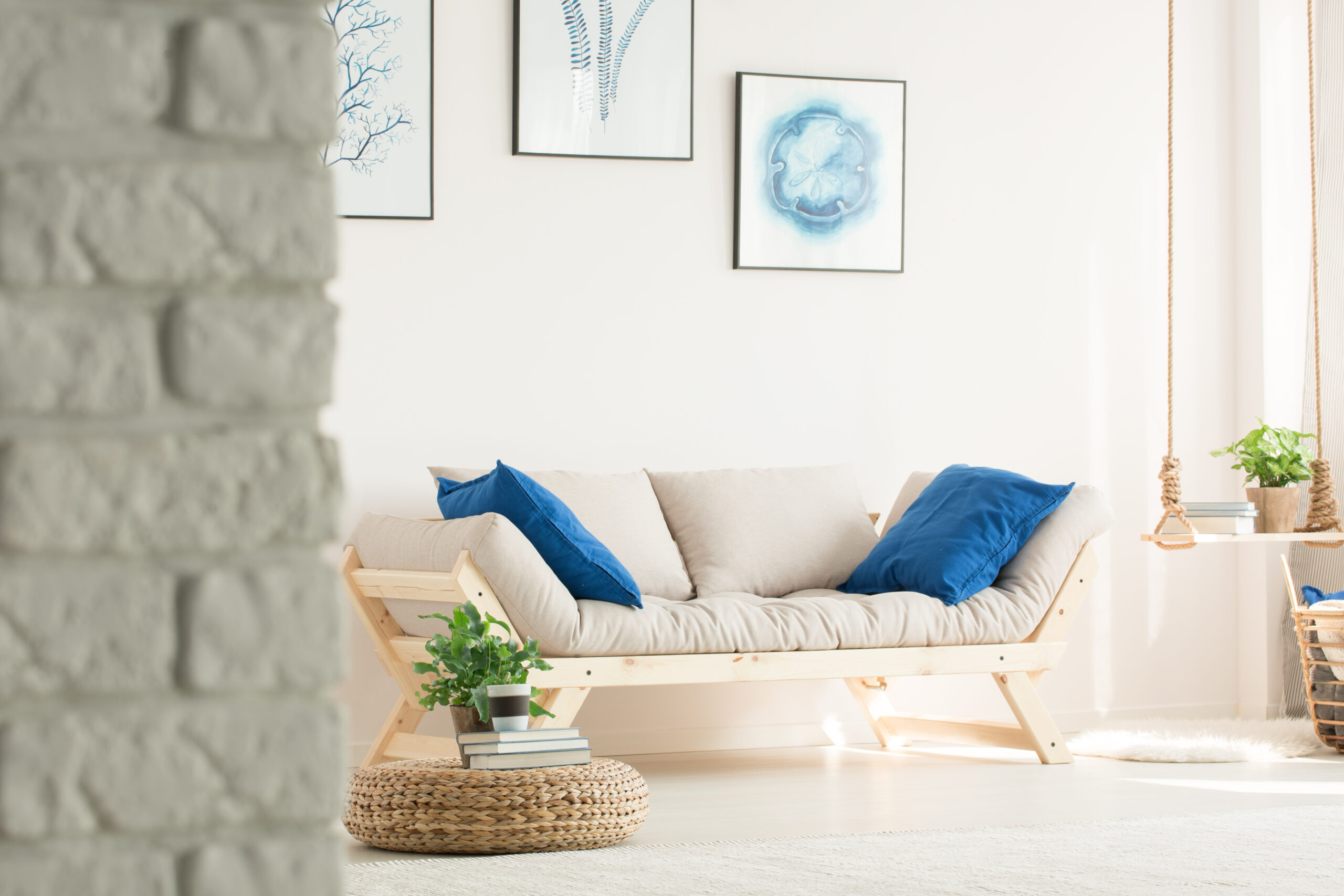 Stylish, white living room with brick wall, wood couch, posters